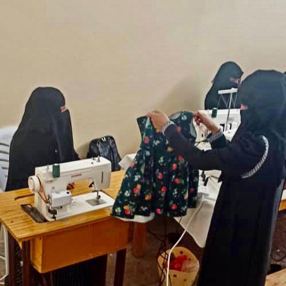A student holding up a floral dress next to a sewing machine